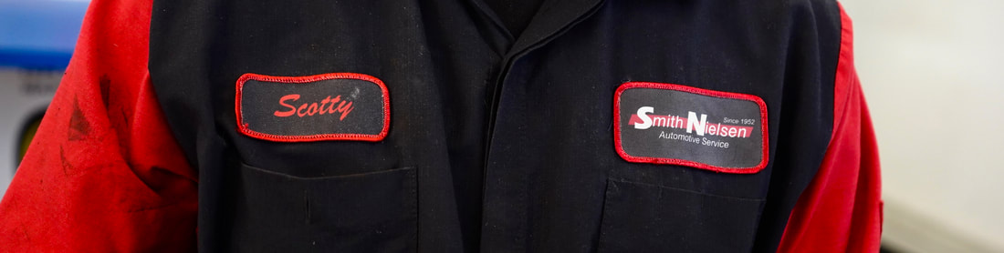 A close up on a red and black work shirt. One patch says Scotty. The other says Smith Nielsen.