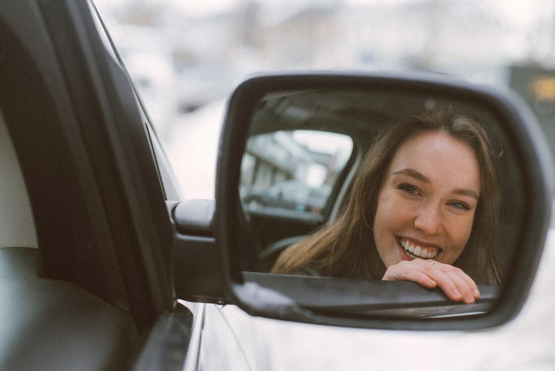 We see a smiling woman's image in the rearview mirror of her car.